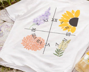 White t-shirt with colorful floral and clock design on grass